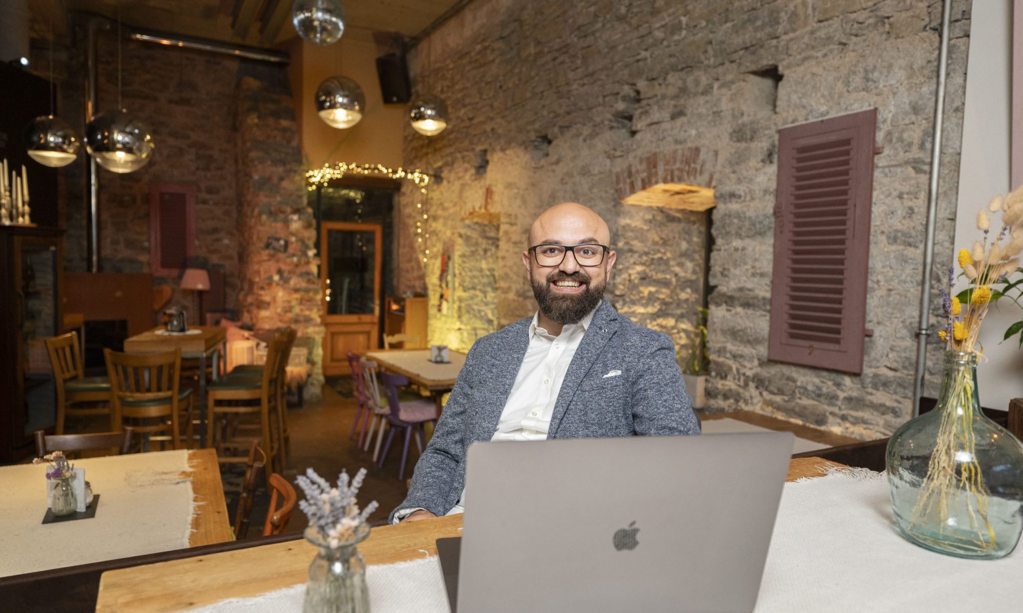 Gökhan sitzt an einem Tresen mit dem aufgeklappten Laptop und lächelt seinem neuen Begleiter entgegen